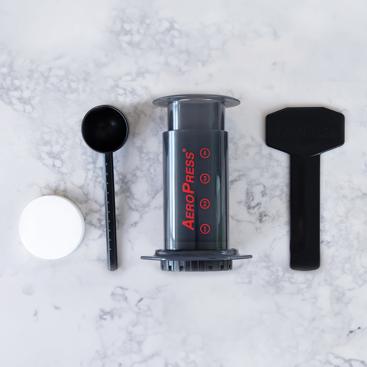 AeroPress Original Coffee Maker with scoop, filter cap, and stirring paddle on marble