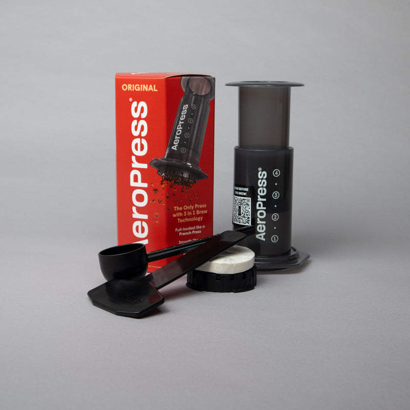 AeroPress Original Coffee Maker with accessories and red branded box on grey background