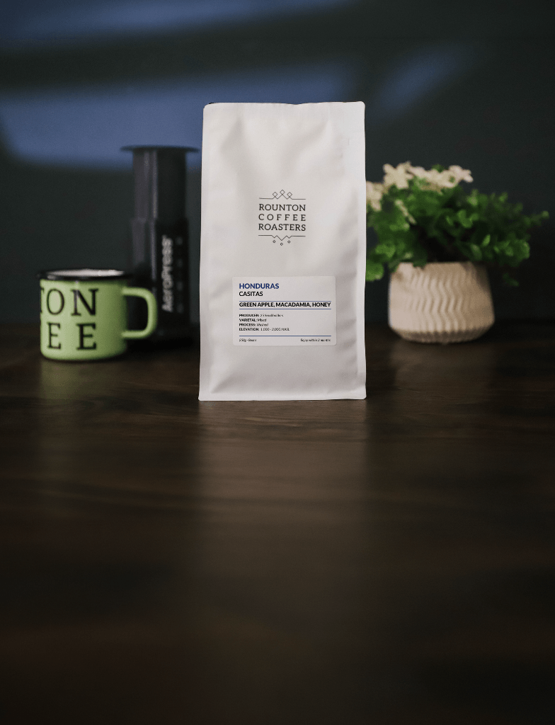 White coffee bag on a wooden table beside a mug and grinder