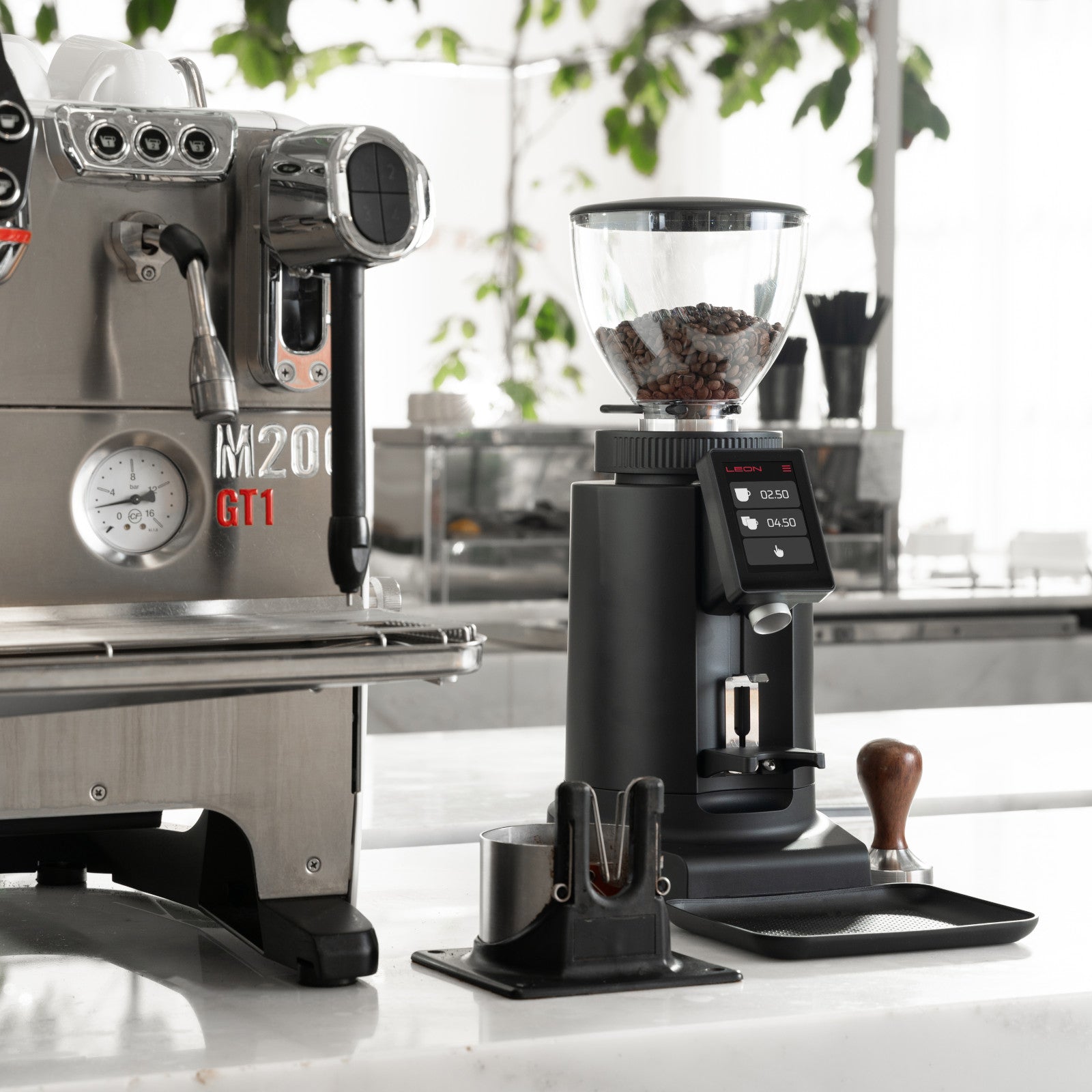 Leon 600 coffee grinder with beans, next to a commercial espresso machine in café setting