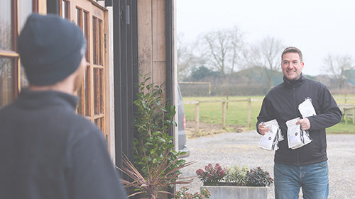 Man delivering coffee bags to a person at the door in a rural setting