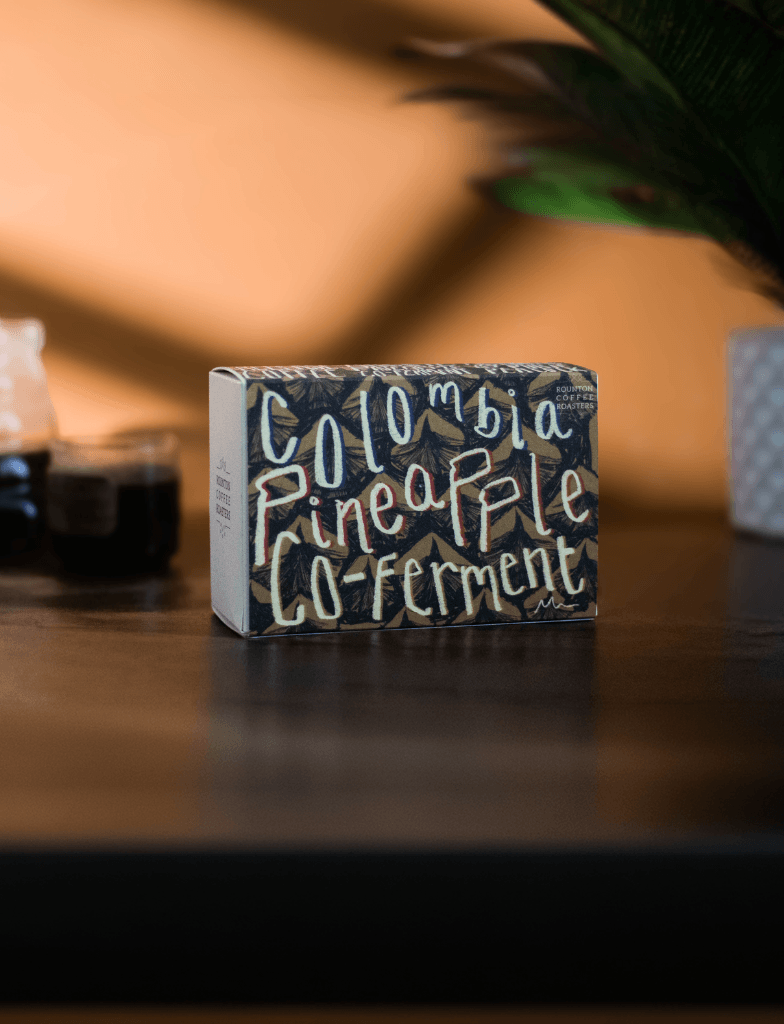Box with handwritten text reading Colombia Pineapple Co-ferment on a wooden surface