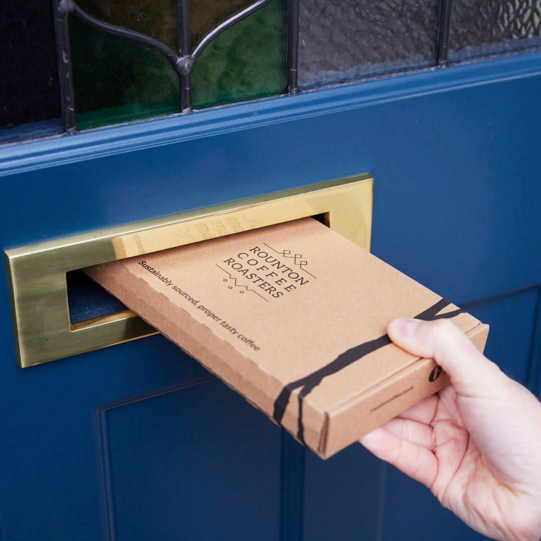Hand delivering a Rounton Coffee Roasters box through a blue door mail slot