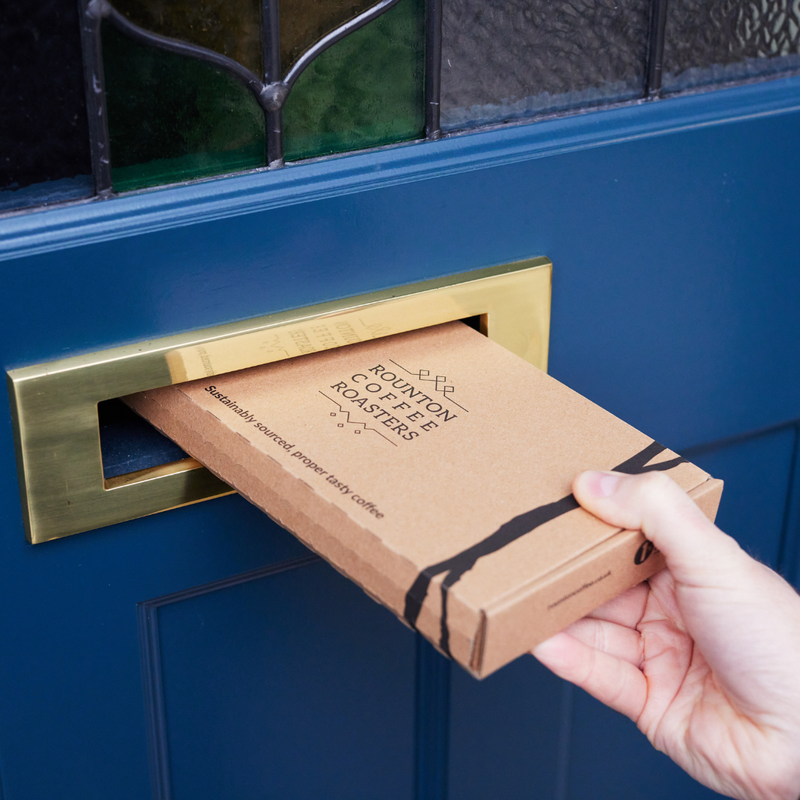 Hand delivering a Rounton Coffee Roasters box through a blue door mail slot